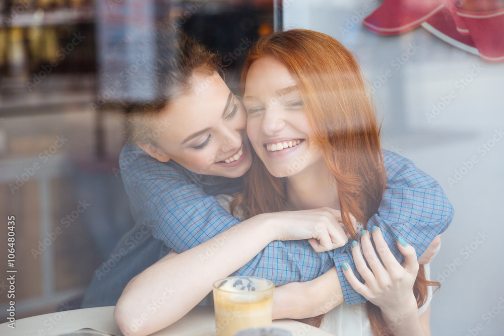 Two cute happy women hugging in cafe Two cute happy women hugging in cafe
