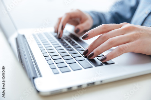 Hands of woman in blue shirt typing on laptop keyboard