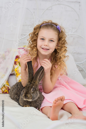 Little curly girl plays with bunny in the bed