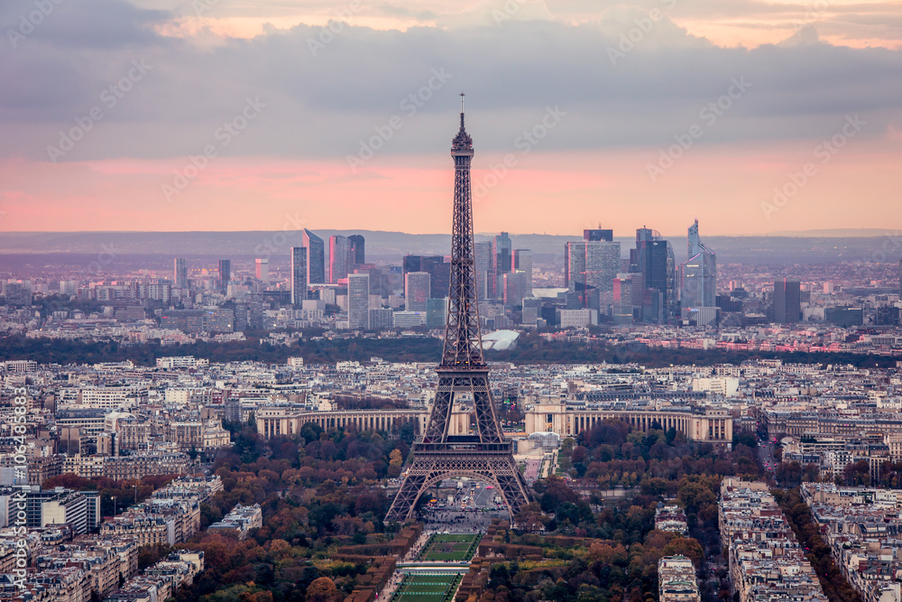 A panorama of Paris at a sunset. A view of the Eiffel Tower, the Defence quarter, of the urban neighborhoods from the bird's-eye view. The sky is clouded over.