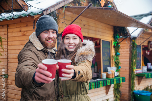 Happy couple offering hot drinks to you on christmas market