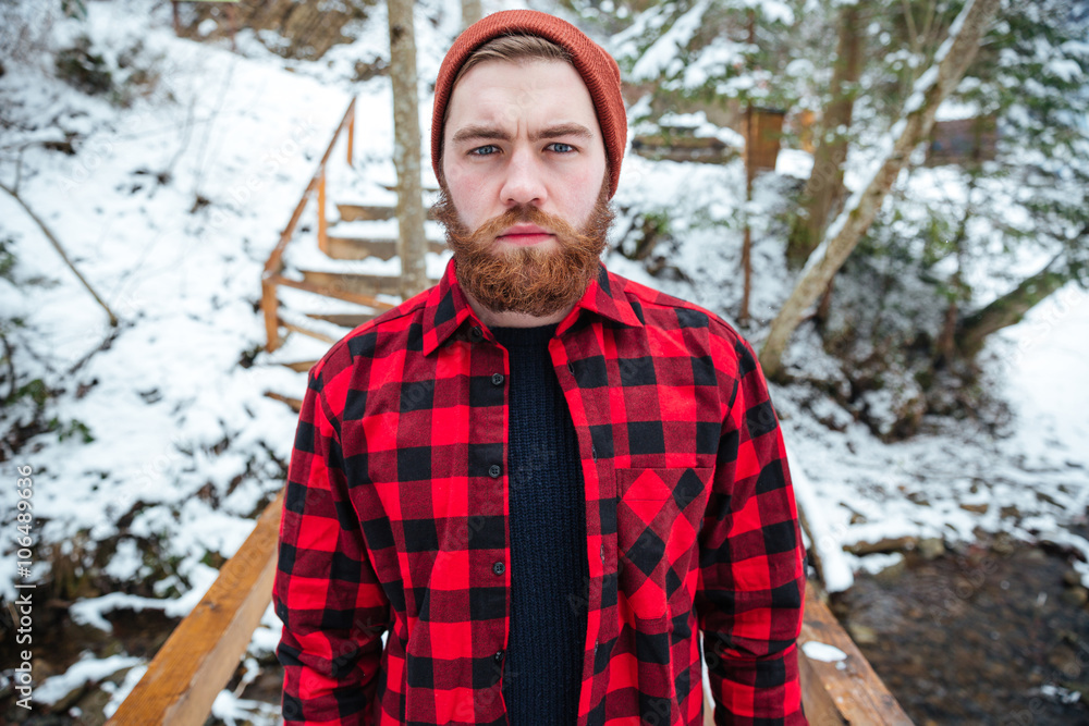 Serious man with beard in plaid shirt at winter forest