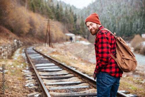 Cheerful man with backpack walking along railroad in mountains