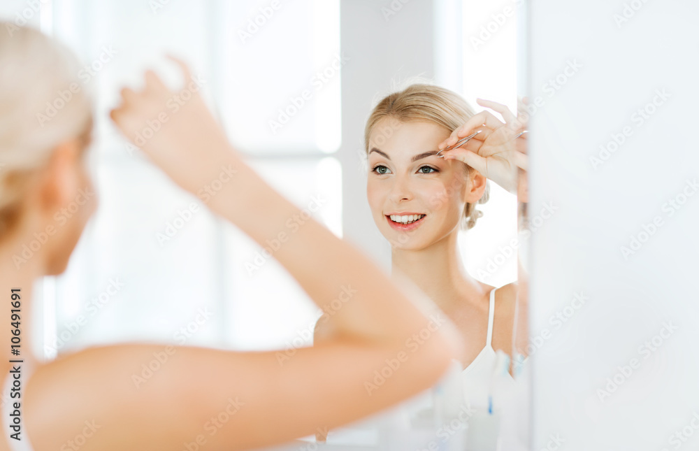woman with tweezers tweezing eyebrow at bathroom