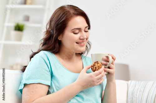 happy plus size woman with cup and cookie at home