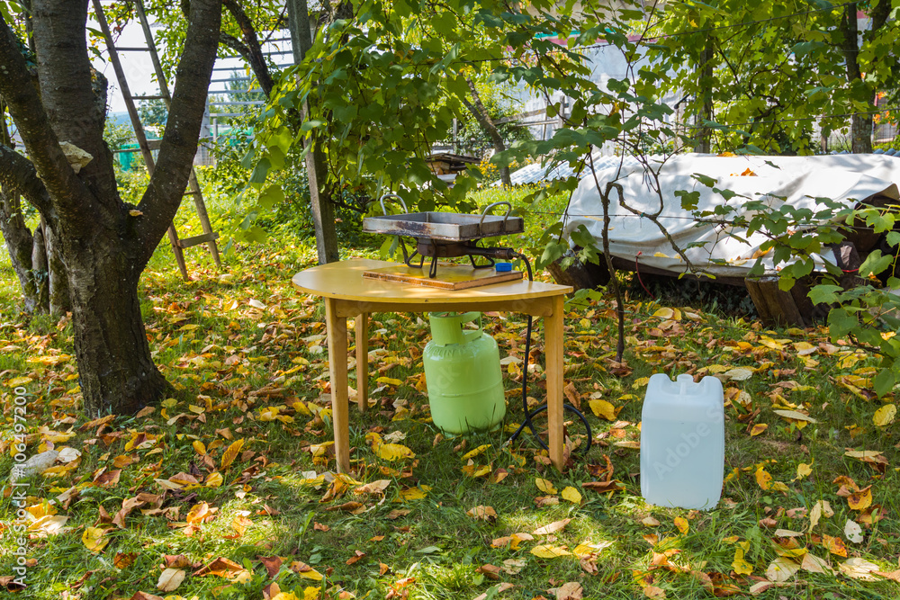 Set up prepared for grill using gas under the tree on the grass covered with yellow leaves. Set up prepared for grill using gas under the tree on the grass covered with yellow leaves.