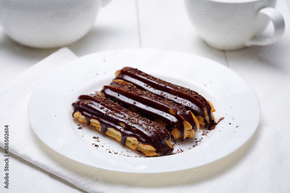 Eclairs or profiteroles with chocolate icing and whipped cream on white dish background. Traditional French dessert.