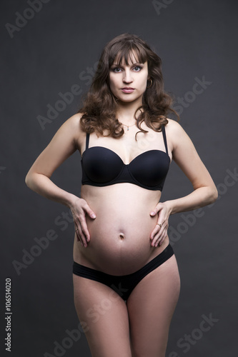 Young beauty and sexy caucasian pregnant woman in black lingerie on gray studio background © staras
