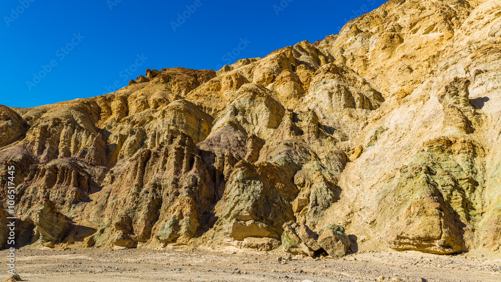 Fototapeta premium High sandstone cliffs painted in many glowing shades of orange, gold and red. Narrow canyon with vertical walls on both sides. Rocky landscape background. Golden canyon, Death Valley