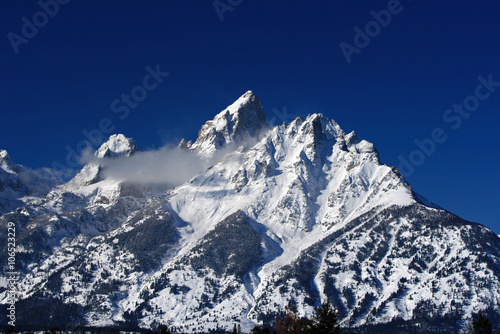 Snow mist blowing off Grand Tetons peaks  in front of snowfield photo