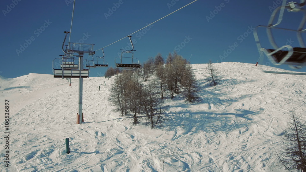 Riding a chair lift in first person view above the ski slope on sunny winter day.
Riding a chair lift in first person view above the ski slope on sunny winter day.
