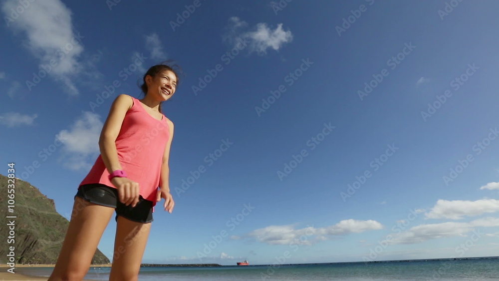 Runner woman using heart rate monitor stopwatch starting watch going running on beach. Sport fitness girl exercising and training outside under blue sky by the sea. Runner woman using heart rate monitor stopwatch starting watch going running on beach. Sport fitness girl exercising and training outside under blue sky by the sea.