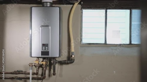 camera moves left from behind a wall to reveal a tankless water heater on the wall in a basement
