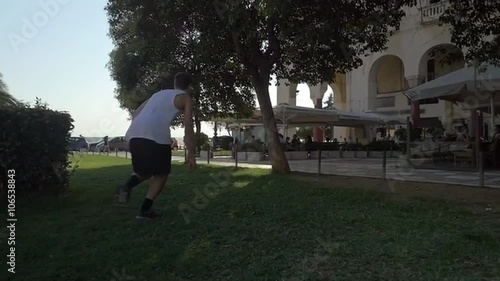 Slow motion steadicam shot of a young sportive man doing parkour in the city. He making somersault pushing off the tree photo