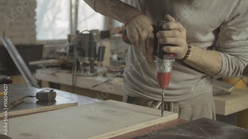 Professional aged carpenter make holes in polished wooden board by drill. Manufactoring. Scobs photo