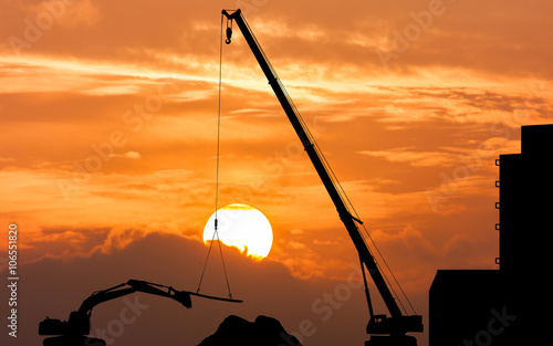 silhouette of excavator and crane working sunset background