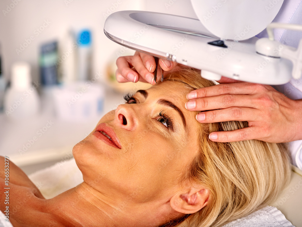 Naklejka premium Woman middle-aged in spa salon with young beautician. Tweezing eyebrow by beautician. Aesthetic medicine.