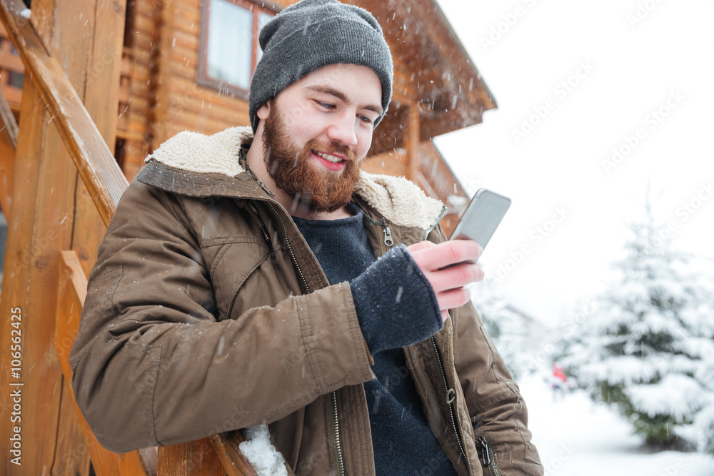 Smiling man standing and using smartphone outdoors in winter Smiling man standing and using smartphone outdoors in winter