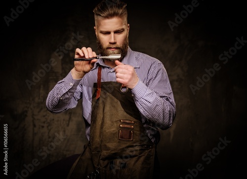 Portrait of stylish barber with beard and professional tools isolated on a dark background.