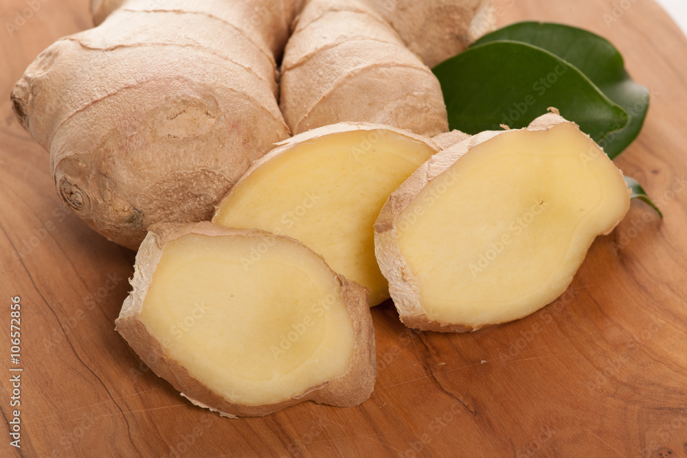 Ginger root slices with green leaves on wooden table. Ginger root slices with green leaves on wooden table.