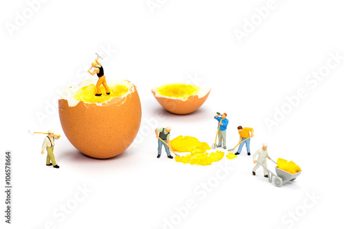 Team of miniature human figurines transporting chicken egg yolk