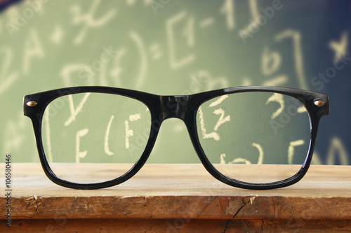 hipster glasses on a wooden rustic table in front blackboard with math formulas and calculation. vintage filtered 