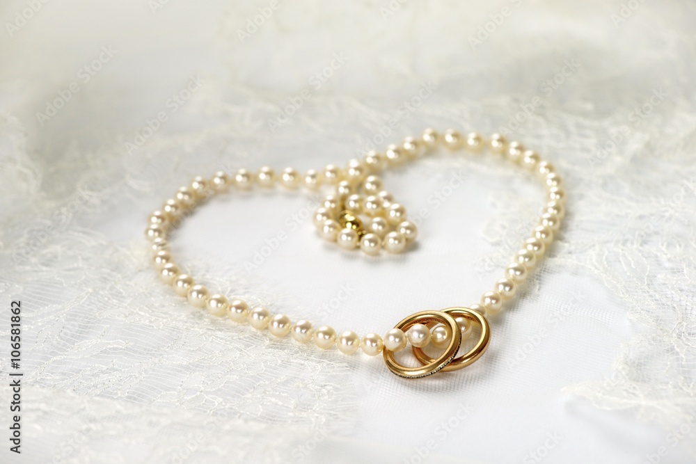 Heart of pearl necklace with two golden rings resting on white wedding lace Heart of pearl necklace with two golden rings resting on white wedding lace