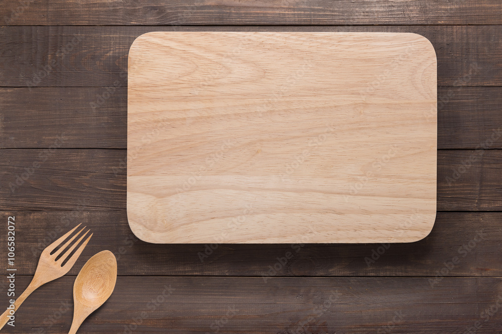 Cutting board, spoon and fork on the wooden background