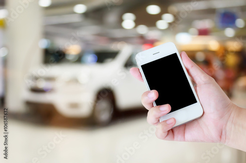 hands holding mobile phone with new cars in showroom