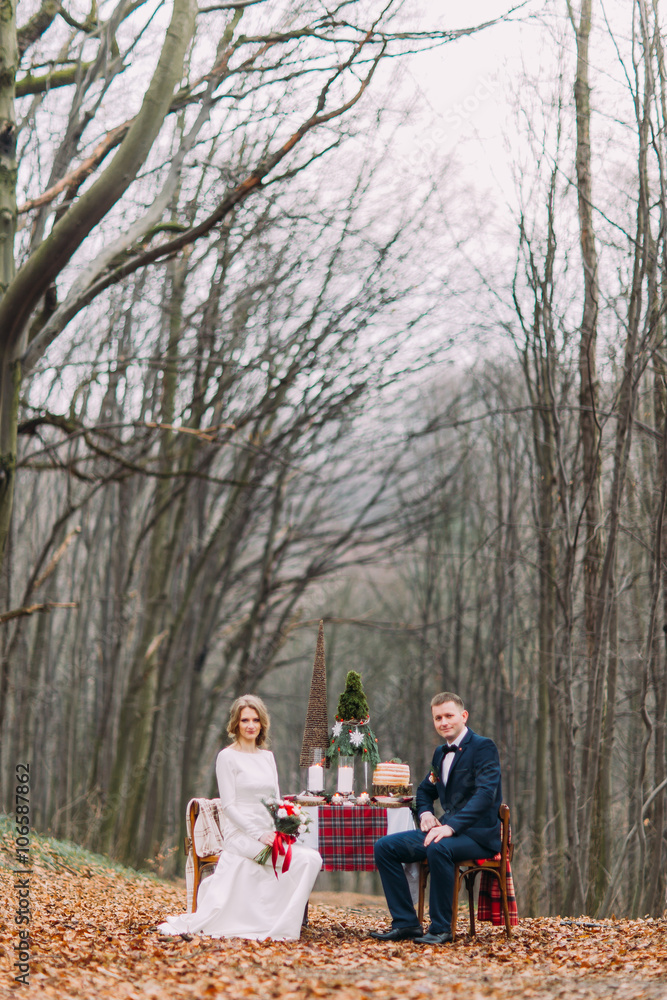 Wedding couple sitting at the holiday table in autumn forest Wedding couple sitting at the holiday table in autumn forest