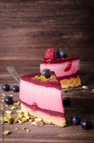 Piece of delicious raspberry cake with fresh raspberries, blueberry, currants and pistachios on shovel, wooden background. Free space for your text. photo