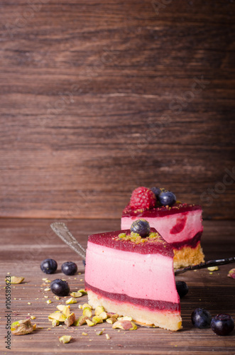 Piece of delicious raspberry cake with fresh raspberries, blueberry, currants and pistachios on shovel, wooden background. Free space for your text. photo