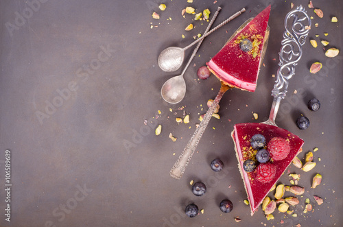 Piece of delicious raspberry cake with fresh raspberries, blueberry, currants and pistachios on shovel, black background. Free space for your text.