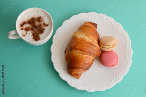 cup of cappuccino with croissant and macarons photo