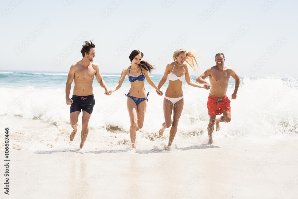 Happy friends holding hands and running on the beach