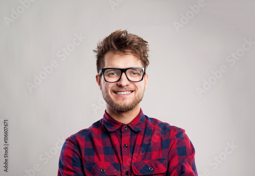 Man in checked shirt and eyeglasses against gray background.