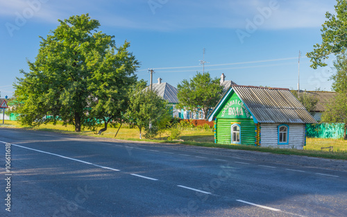 Fototapeta Naklejka Na Ścianę i Meble -  Summer landscape with big pear-tree and  draw-well as a small wooden house at roadside in Lyubka village, Sumskaya oblast, Ukraine