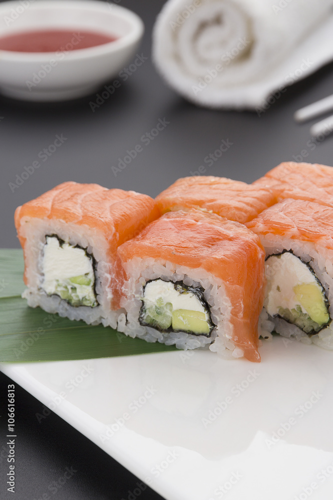 Japanese cuisine. Salmon sushi on a wooden plate with ginger wasabi and sauces over black background Japanese cuisine. Salmon sushi on a wooden plate with ginger wasabi and sauces over black background
