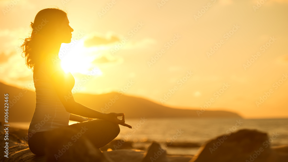woman meditating in lotus pose on beach at sunset - obrazy, fototapety, plakaty 