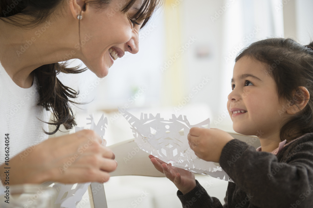 Hispanic mother and daughter making paper snowflakes Hispanic mother and daughter making paper snowflakes