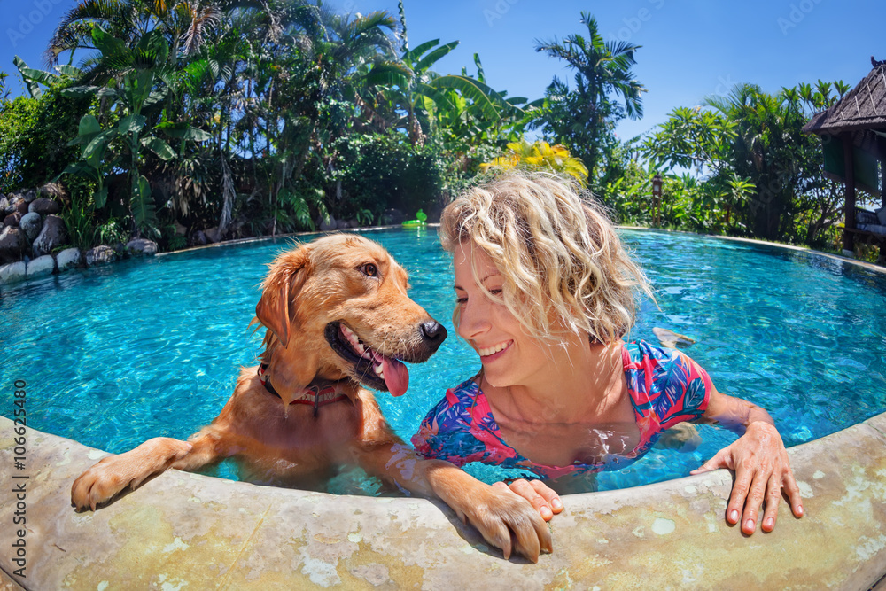 Fotka „Funny portrait of smiley woman playing with fun and training golden  retriever puppy in outdoor swimming pool. Popular dog like companion,  outdoor activity and game with family pet on summer holiday.“ ze