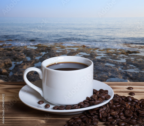 Coffee beans and coffee in white cup on wooden table opposite a