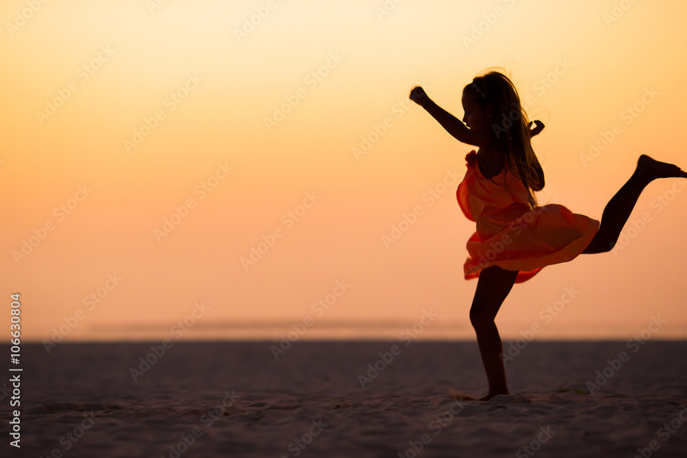 Silhouette of sporty little girl on white beach at sunset