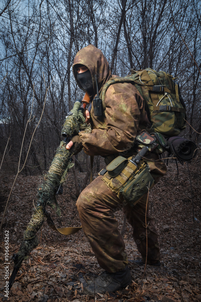 Sniper wearing camouflage suit with rifle walk in the woods