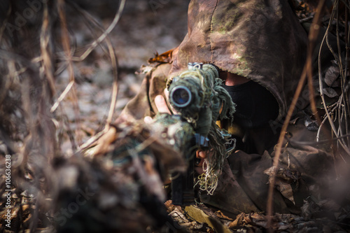 Sniper wearing camouflage suit with rifle hide in the woods © Mrakor