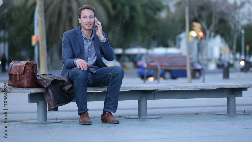 Smart phone man talking and texting in city night using smart phone. Handsome young business man smiling happy wearing suit jacket. Urban male professional in his 20s in Barcelona, Spain. Smart phone man talking and texting in city night using smart phone. Handsome young business man smiling happy wearing suit jacket. Urban male professional in his 20s in Barcelona, Spain.