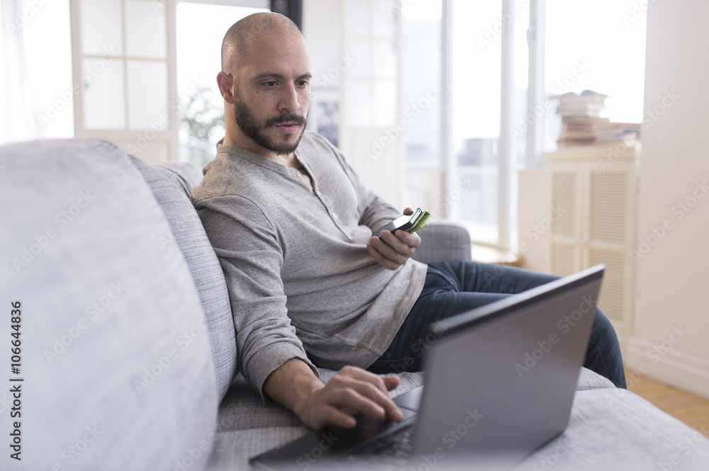Hispanic man using cell phone and laptop on sofa Hispanic man using cell phone and laptop on sofa