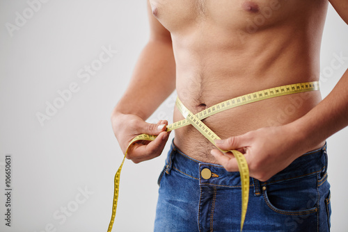 Cropped image on man measuring his waist with tape photo