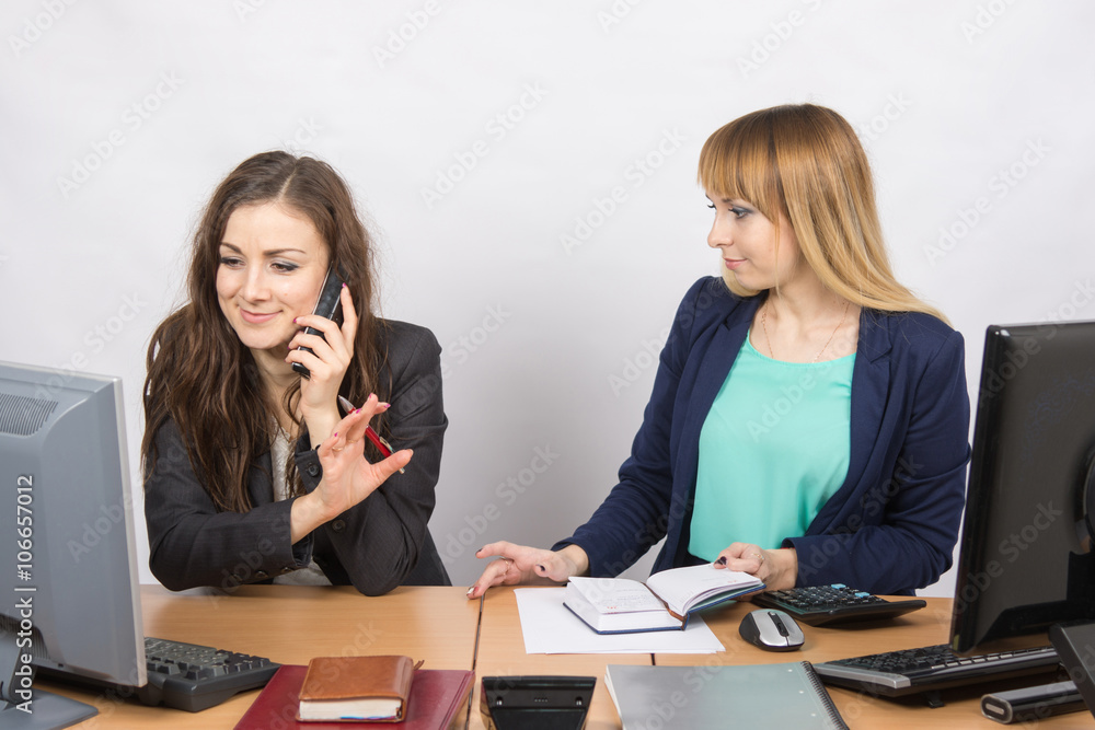 The girl in the office talking on the phone asking a colleague to wait The girl in the office talking on the phone asking a colleague to wait