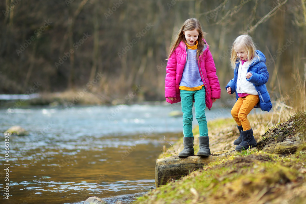 Two cute little sisters playing with a stick by a river Two cute little sisters playing with a stick by a river